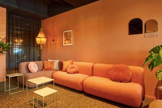 Modern zithoek met rood-oranje modulaire bank, bruine zijstoel, gouden hanglamp en gele bijzettafels op kurkvloer tegen oranj