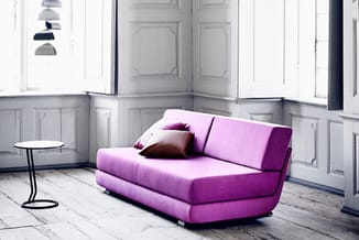 Roze modulaire slaapbank met drie zitkussens in minimalistische witte kamer met houten vloer, bijzettafel en hanglamp.