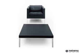 Zwarte lederen fauteuil en zwarte salontafel met metalen frame op witte achtergrond.