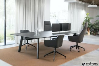 Moderne vergaderruimte met zwarte rechthoekige tafel, grijze bureaustoelen met wieltjes, monitor op standaard, potplanten en