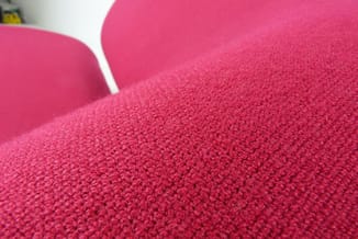 Roze stofbeklede kantoorstoel met textieloppervlak en ergonomische rugleuning, detail van materiaalstructuur.