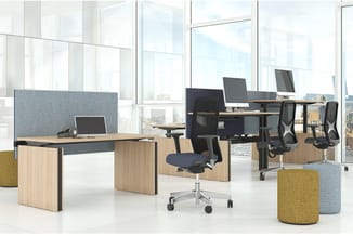 Modern kantoor met houten bureaus, grijze akoestische schermen, zwarte ergonomische stoelen, gele poef en grote ramen met sta