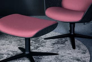 Twee roze stoelen met zwarte poten op een grijze vloerkleed in een kantooromgeving met donkere wanden.