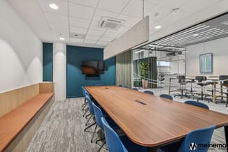 Moderne vergaderruimte met houten vergadertafel, blauwe stoelen, blauwe muursegment, zitbank met oranje kussen, glazen wand e