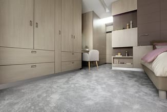 Moderne slaapkamer met lichte houten kasten, wit dressoirmeubel met spiegel, grijze betontegel vloer en witte fauteuil met ho
