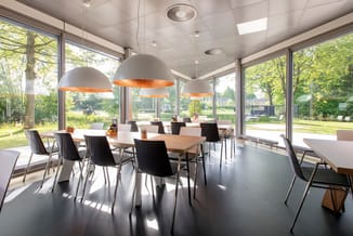 Moderne kantoorruimte met witte hangende lampen met koperkleurig interieur, houten en wit tafelblad, zwarte stoelen, grote ra