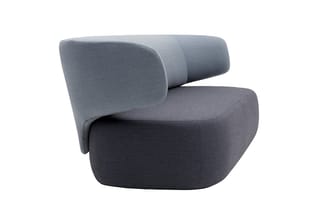 Grijze fauteuil met ronde vormen, gebogen armleuning en cilindervormige rugkussen, geïsoleerd op witte achtergrond.