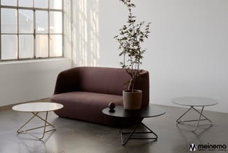 Donkerbruine gesloten bank met ronde vormen, omgeven door drie bijzettafels met metalen poten in een minimalistisch interieur
