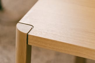 Houten tafelhoek met afgeronde rand en donkere inleg, detail van massief houten constructie.