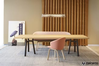 Vergaderruimte met houten tafel, zwarte poten, roze stoel, beige achterwand, gouden gordijnen, hanglampen en kunstwerk met vo