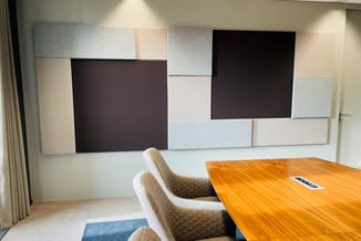 Houten vergadertafel met grijze gestoffeerde stoelen en grote akoestische wandpanelen in zwart, grijs en wit.