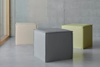 Drie gesloten kasten in verschillende kleuren (beige, donkergrijs, geel-groen) op betonachtige vloer tegen grijze muur.