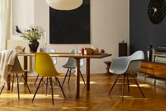 Houten eettafel met gele en grijze kunststof stoelen met zwart metalen frame, in modern ingerichte woonkamer met houten vloer