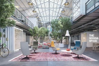 Modern kantoorlandschap onder glazen koepel met grijze en gele loungestoelen op roze tapijt, groene planten, witte hanglamp e