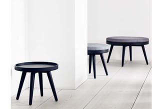 Drie zwarte houten bijzettafels met grijze textielkussens en donker blad, opgesteld in een heldere kantoorruimte op houten vl