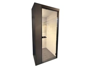 Zwarte akoestische belcel met glazen deur, crèmekleurig interieur en grijze vloer.
