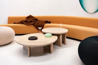 Houten salontafels met lichte afwerking in moderne woonruimte met geel/oranje zitbank, poefjes en glazen accessoires.