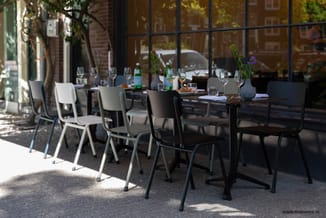 Buitenzonnetuin met zwarte vergadertafel en moderne stoelen in wit en zwart, voorzien van glazen en bloemenvazen.