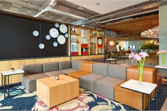 Modern kantoorlounge met grijze en oranje modulaire bank, houten salontafel, decoratieve borden aan muur, houten wandplanken