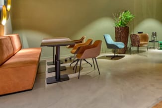 Ingerichte kantoorruimte met oranje lederen bank, houten tafel met oranje stoelen, lichtblauwe fauteuil, plantenbakken en wan
