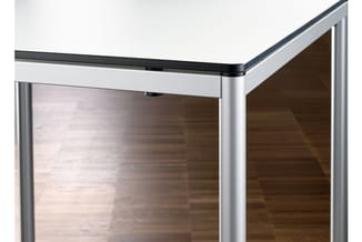 Hoekdetail van een moderne glazen wand met zilverkleurig aluminium frame en donker afwerkingsgedeelte bovenaan.