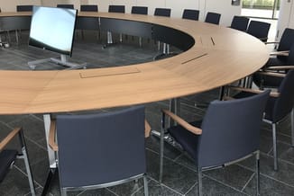 Halfronde vergadertafel in licht houtfineer met ingebouwde schermen, omgeven door donkerblauwe conferentiestoeLen in moderne