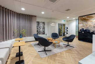 Modern kantoorinterieur met drie zwarte fauteuils, houten bijzettafel, grijze ruit, houten tafels, grijze gordijnen en abstra