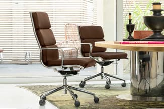 Bruine leren bureaustoel met chromen frame en wielen in modern kantoor met hoge ramen en blinds.