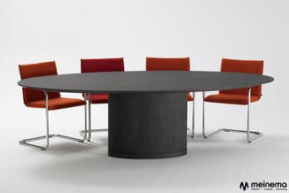 Zwarte ronde vergadertafel met vier bruine kantooorstoelen met chromen frames, gepositioneerd in vergaderruimte.