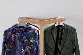 Houten kledingrek met gebogen bovenbalk waaraan twee jasjes hangen: een blauw jasje met vogelpatroon en een donkergroen jasje
