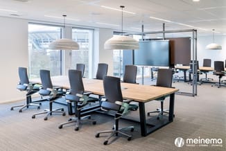 Moderne vergaderruimte met houten tafel, zwarte bureaukstoelen, hangende zilveren lampen en glazen scheidingswanden.