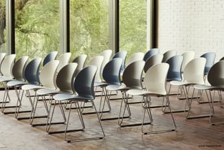 Moderne stoelen in wit, beige en donkergrijs met gebogen rugleuning op sledepoten, opgesteld in rijen voor een raam met uitzi
