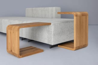 Grijze zitbank met houten armleuningen en zwart metalen onderstel, geflankeerd door twee houten bijzettafels met gebogen vorm