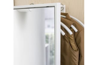 Witte garderobe met stang waaraan bruine jassen op witte hangers hangen, tegen houtstructuur wand.