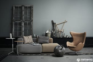 Moderne woonkamer met grijze modulaire bank, cognackleurige eggchair, houten bijzettafel, grijs tapijt en industriële ramen t