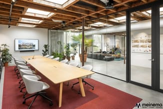 Moderne vergaderruimte met houten vergadertafel, witte bureaukstoelen, rode vloerbedekking, glazen wanden en houten balkenpla