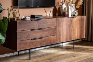 Houten tv-meubel in walnootkleur met drie laden en twee kastdeuren, op zwart metalen onderstel, met TV en decoratie.