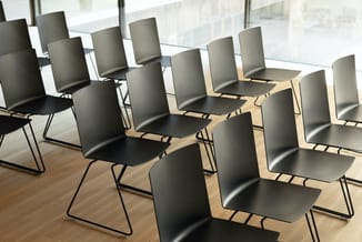 Zwarte kantooorstoelen met metalen frame in rijen opgesteld in een moderne ruimte met houten vloer en grote ramen.