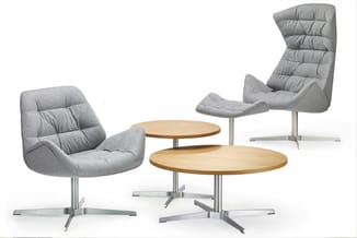 Grijze loungestoelen met quilting en houten salontafels op metalen kruisvoeten, minimalistisch kantoorinterieur.