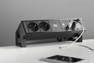 Zwarte bureau-stroomstrip met twee stopcontacten, USB-lader en kabelorganizer, staand op witte ondergrond.