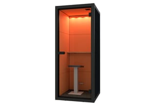 Akoestische belcel met zwart frame, oranje interieurwanden, enkele stoel en kleine tafel, verlicht plafond.