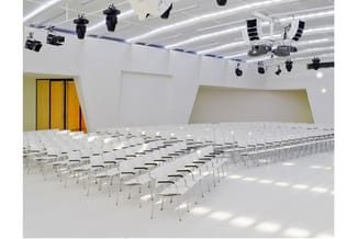 Moderne presentatieruimte met witte stoelen in rijen, gele en groene wanden, afgesloten plafond met professionele verlichting