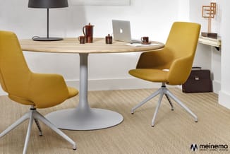 Ronde tafel met houten blad op wit voetsteuk met twee gele stoelen met grijze poten, op beige tapijt in moderne kantoorruimte