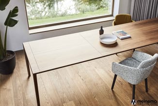 Moderne vergadertafel met uitschuifblad in natuurlijk hout, grijze stoel, potplant en grote raampartij met uitzicht op groen.