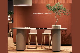 Moderne kantoorinrichting met lange tafel met geribbelde witte zuilen, twee roze barkrukken, bonsai in pot, terracotta muur e