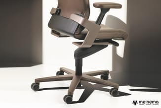 Ergonomische bureaustoel in taupe/beige met zwarte armleuningen, zitjuk en wielen, draaionderstel, tegen lichte achtergrond.