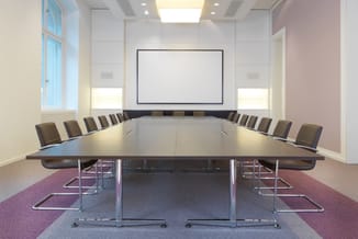 Moderne vergaderkamer met lange zwarte tafel, bruine stoelen met metalen frame, whiteboard aan wand, raam en inbouwverlichtin