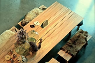 Houten vergadertafel met naturel fineer, beklede zitblokken met bruine en beige bont, glazen vaas met droogbloemen, houten ac