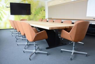 Moderne vergaderruimte met lichte houten tafel, cognackleurige gestoffeerde stoelen op wielen, whiteboard, TV-scherm en groen