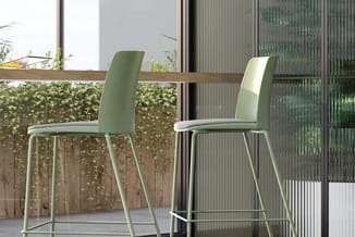 Twee groene barkrukken met grijze zitting aan houten bartafel op terras met klimopbeplanting en raampartijen.
